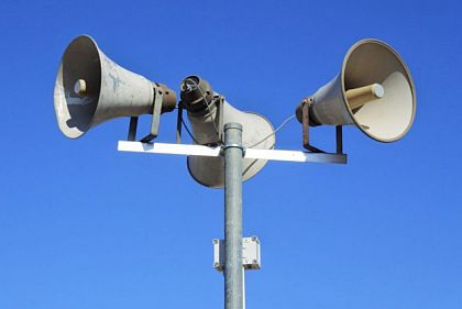 Громкоговорители системы оповещения на столбе на фоне голубого неба