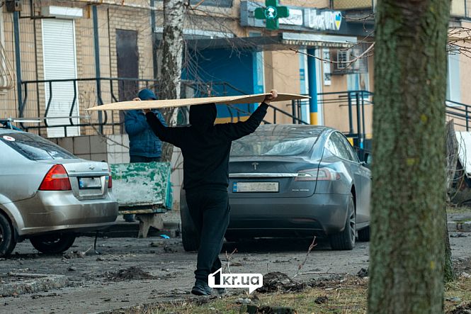 людина несе дсп щоб залатати вікна після обстрілу зробленого російською федерацією